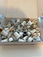 Top view of a box filled with approximately 36 assorted small ceramic thimbles in varying designs, colors, and shapes.