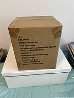 Photo of sealed cardboard box showing product details: Wolfgang Puck WP 1.5 cup portable cooker, green color, measuring 193x193x227 mm, 1.3 kg, made in China.