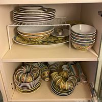 Top and bottom shelf cabinet view showing full set of plates, bowls, cups and spoons