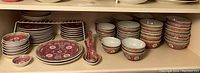 Photo showing multiple stacks of small and large bowls, flat dinner plates, small dipping plates and Asian-style spoons with intricate red, white, and green patterns.