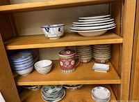 Top shelf displaying one blue-and-white porcelain bowl with dancer motif and stack of six white shallow dishes