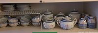 Wide shelf view showcasing stacked teacups, saucers, and three teapots with floral and geometric blue-white patterns.