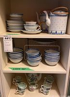 Wide shot showing the teapots on the right, stacked saucers and bowls on the left, small cups below.