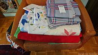 Stack of bed linens including pillowcases, sheets, and a quilt on an orange chair showing mix of patterns and colors.