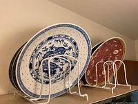 Side view of 5 plates standing vertically in a rack, showing blue dragon design and red patterned design plates.