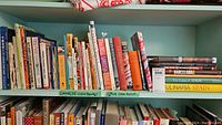 Shelf with mostly Chinese cookbooks and some Spanish cooking books, showing colorful and various sized cookbooks.