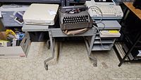 Gray metal desk on casters holding three typewriters