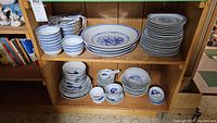 Shelf with stacks of blue and white porcelain dishes and bowls, some with floral and traditional blue patterns.