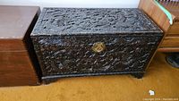 Full view of the dark wood chest showing carved dragon design on lid and front and circular metal lock plate.