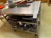 Full view of stainless steel kitchen cart with three shelves, loaded with some kitchenware and other items on top and bottom shelves.