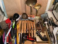 Various kitchen utensils arranged together including knives, tongs, spatulas, ladles, sharpeners, and other tools.