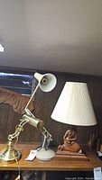 Two desk lamps on wooden shelf: brass trombone lamp and wooden sculpture base lamp with shade