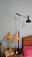 Three lamps grouped: one tall floor lamp and two smaller desk lamps on a bedside table.