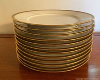 Stacked set of 12 Limoges porcelain plates showing gold trim detail on rim.
