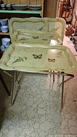 Front view of four folded handi-tables stacked with butterfly design trays.
