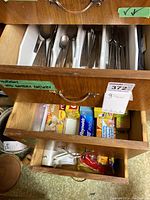 Wooden kitchen drawers containing Norway mid century stainless steel cutlery organized in white plastic inserts. Second drawer contains various kitchen disposables including freezer bags and wraps.