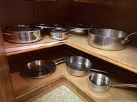 Assortment of stainless steel pots and pans with lids on wooden shelves