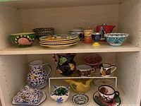 Hand painted pottery dishes, bowls, mugs, and pitchers on wooden shelves, showing colorful artisan patterns
