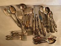 Full set of tarnished 1881 Rogers Oneida Ltd. flatware arranged on white surface showing spoons, forks, knives, and serving pieces with ornate decorative handles.