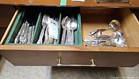 Drawer with multiple compartments holding numerous forks, spoons, and cutting tools, all silver plated with matching ornate handles.