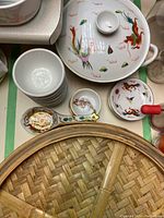 Close-up of porcelain soup spoons, bowls, and lidded serving dish with dragon and phoenix patterns arranged around bamboo steam basket.