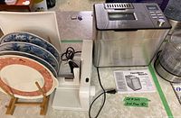Plates on wooden rack with electric meat slicer and Hamilton Beach bread maker.