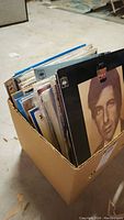 Cardboard box filled with assorted vinyl LP albums, Leonard Cohen cover visible at front