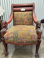 Front view of the antique chair showing carved angel heads on armrests and patterned upholstered seat.