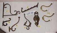 Full display of all 8 antique styled coat hooks and brackets on a white surface labeled Lot 30.