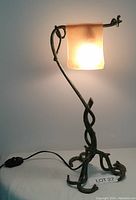 Full view of the wrought iron table lamp illuminated, showing design and amber glass shade.