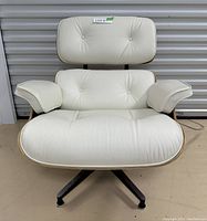 Front view of white leather Eames-style lounge chair showing button-tufted seat and back cushions, armrests, plywood shell, and metal swivel base
