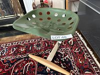 Green perforated metal seat with circular cutouts, curved edges, mounted on wood and chrome frame