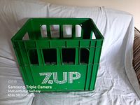 Front and side angle views of vintage 7Up green plastic crate with white branding text '7Up' and 'The Uncola!'.