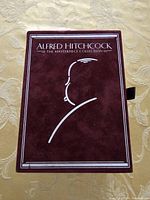 Front view of maroon velvet box with silver embossed silhouette and title 'Alfred Hitchcock The Masterpiece Collection'