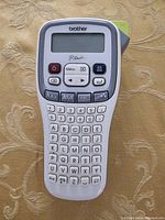 Front view of the Brother PT-H100 label maker showing the LCD display, keyboard layout, and function buttons.