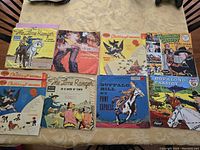 Eight vintage children's 7-inch 45 RPM record covers laid out on a table. Titles include The Lone Ranger, Buffalo Bill, Hopalong Cassidy, Gunsmoke, and Childcraft Records. Covers show age wear and some tears.