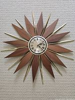 Full view of the Phinney Walker mid century starburst clock showing the wooden and brass starburst rays with the circular clock face centered.