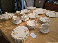 Wide shot of various china pieces on table showing plates, cups, creamers, and covered sugar bowls.