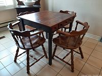 Rustic wooden kitchen table with four spindle back wooden chairs around it, showing the full set and table drawers.