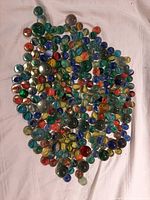 Photo showing a large assortment of glass marbles spread out on a white cloth, highlights variety of colors and sizes.