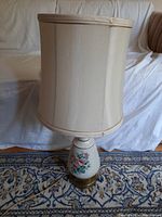 Full view of the lamp showing ceramic base with floral design and lampshade on a patterned carpet background.