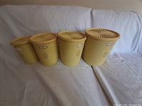 Four vintage yellow Tupperware containers with lids arranged in size order on white sheet.