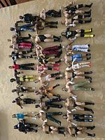 Wide shot of over 40 WWE wrestling figures laid out on a beige surface, showing a variety of wrestlers in different poses and outfits including black, red, yellow, and blue trunks and boots.