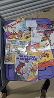 Five assorted Calvin & Hobbes comic books stacked on a purple plastic container lid, showing full front covers.