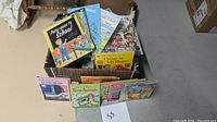Box of assorted baby books showing titles like Peter Goes to School, Things in My House, and several more.