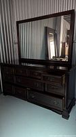Full view of dark stained solid mahogany dresser with a large rectangular mirror on top showing multiple drawers and traditional metal hardware.