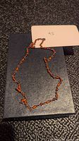 Amber bead necklace laid on a dark textured surface with a price tag showing "Q5".
