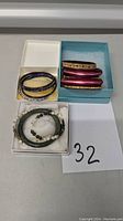 Photo of assorted bracelets including jade bead bracelet, green bead bracelet, two dark bangles, and three maroon bangles with gold-tone design in boxes.