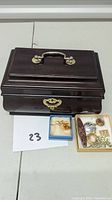 Closed wooden jewelry box, dark polished wood with brass handle and clasp. Jewelry items include various pins and brooches displayed beside the box.