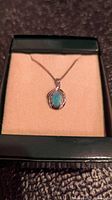 Sterling silver opal pendant on chain displayed in a green jewelry box with cream interior.